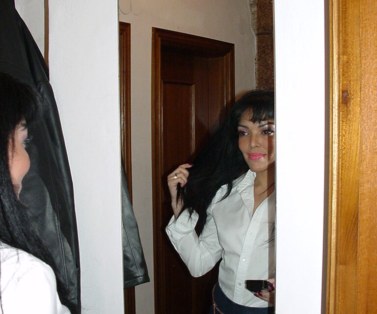 Frau in weißer Bluse blickt sich im Spiegel an